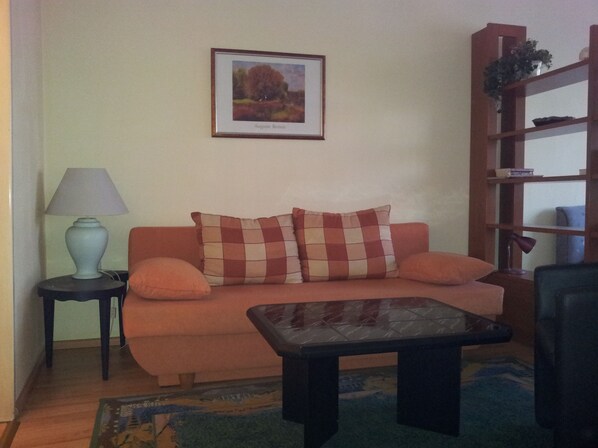 A living room with a sofa, a small table, a lamp, a bookshelf, and a framed picture on the wall.