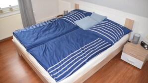 A neatly made bed with blue bedding and pillows, a bedside table with a lamp, and a window with a view of the outdoors.