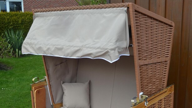 A wooden outdoor seating area with a bench and a table, a covered section with a cushion, and a lamp post in the background.