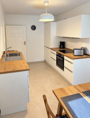 A modern kitchen with white cabinets, a wooden countertop, a built-in oven, and a coffee maker.