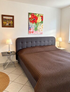 A bedroom with a large bed, two bedside lamps, a framed picture on the wall, and a floor lamp.