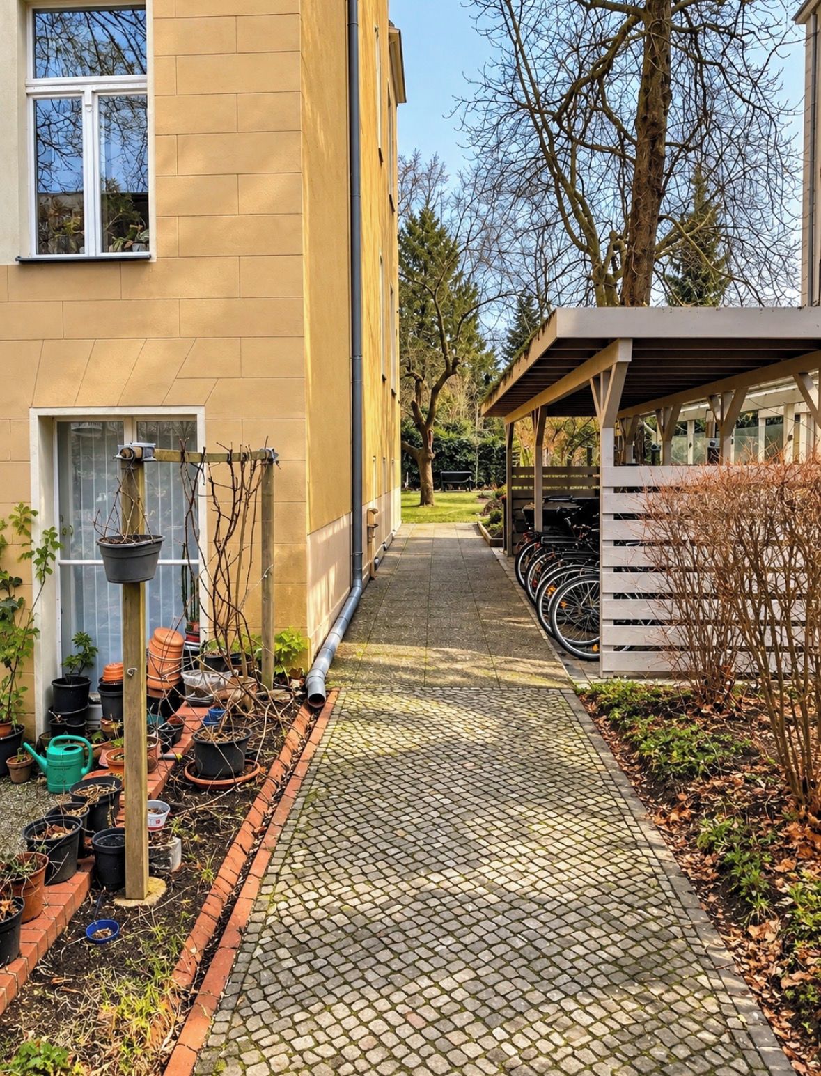 A pathway leading to a building with a covered area, potted plants, and bicycles.