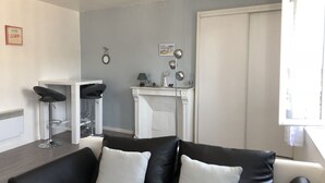 A modern living room with a black leather sofa, a white fireplace, and a dining area with a white table and two black bar stools. - BEAUTIFUL APARTMENT 2 STEPS FROM THE BEACH / NEAR TO THE BEACH! (Étretat)