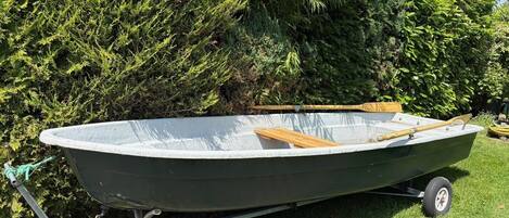 A small, green motorboat with a wooden interior, parked on a trailer in a grassy area with dense green foliage in the background.
