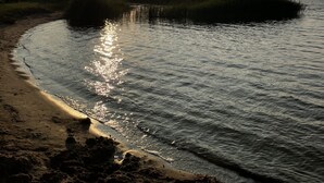 Ein Sonnenuntergang über ruhigem Wasser mit einem Sandstrand und grünen Flächen.