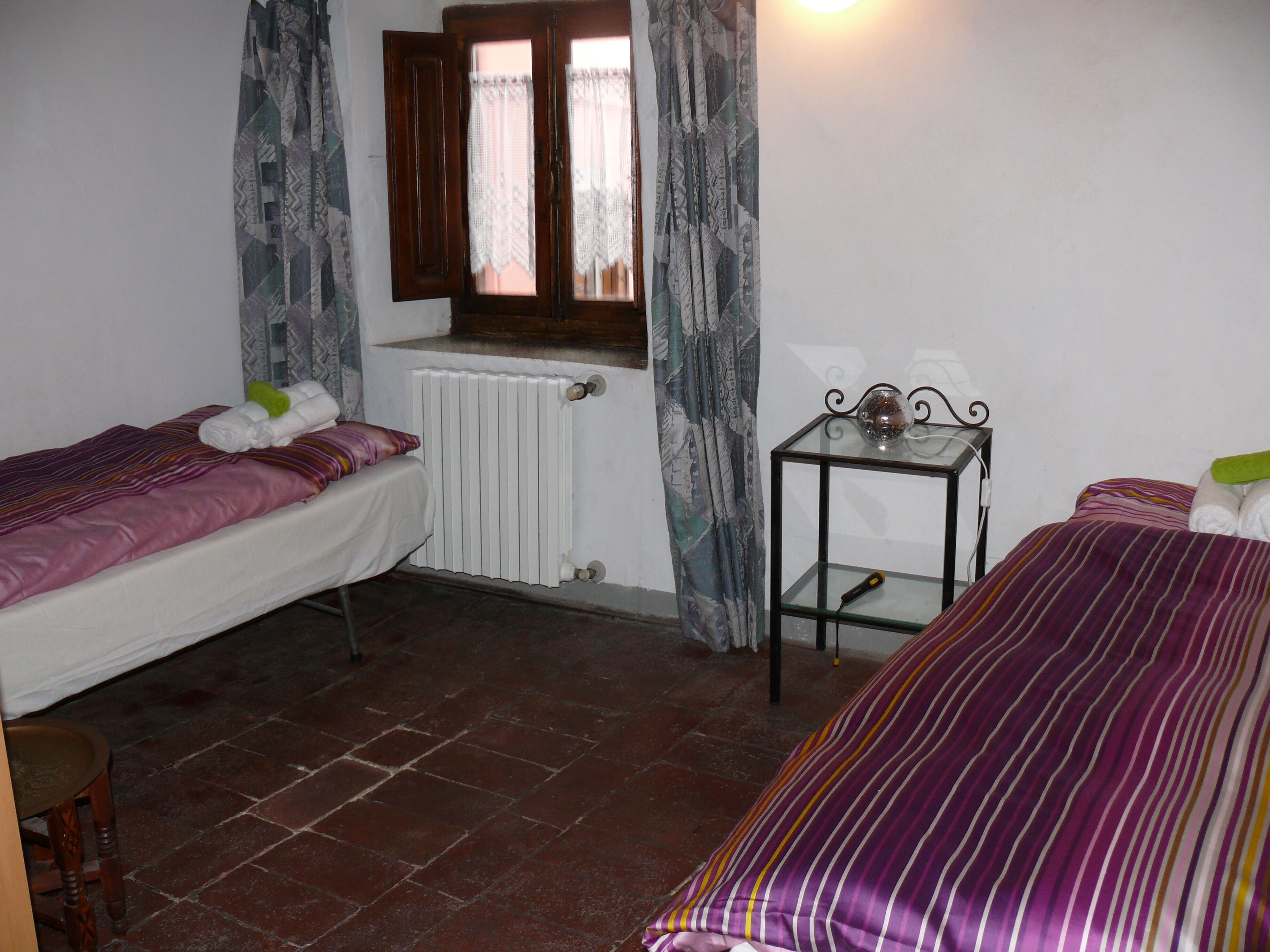 Une chambre avec deux lits, un radiateur, une table avec un plateau en verre et une fenêtre avec des rideaux.