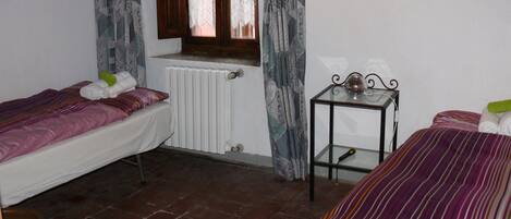 Une chambre avec deux lits, un radiateur, une table avec un plateau en verre et une fenêtre avec des rideaux.