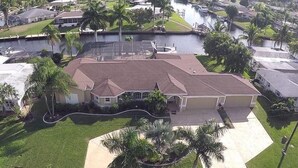 A residential area with a house featuring a large driveway, a swimming pool, and a well-maintained lawn. - Large private saltwater pool with dock, GoM access (Cape Coral)