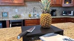A kitchen with wooden cabinets, a granite countertop, a knife, a cutting board, and a pineapple. - Large private saltwater pool with dock, GoM access (Cape Coral)