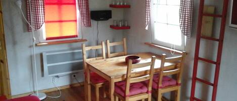 A dining area with a wooden table and chairs, checkered curtains, a window with a view, and a ladder against the wall.