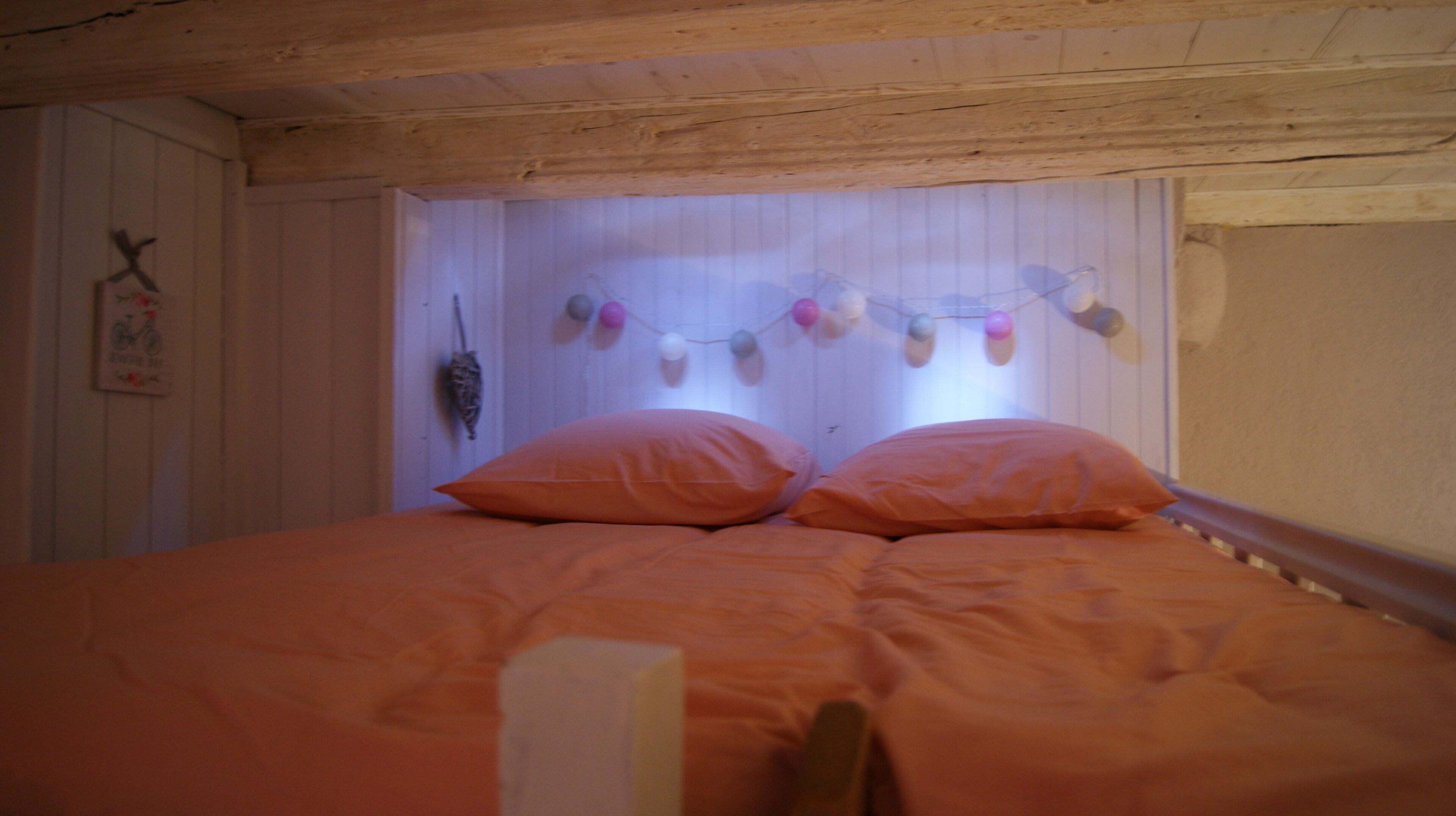 Una habitación con techo de madera, cama con ropa de cama naranja y decoración en la pared con adornos colgantes.