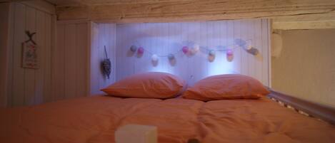 Una habitación con techo de madera, cama con ropa de cama naranja y decoración en la pared con adornos colgantes.