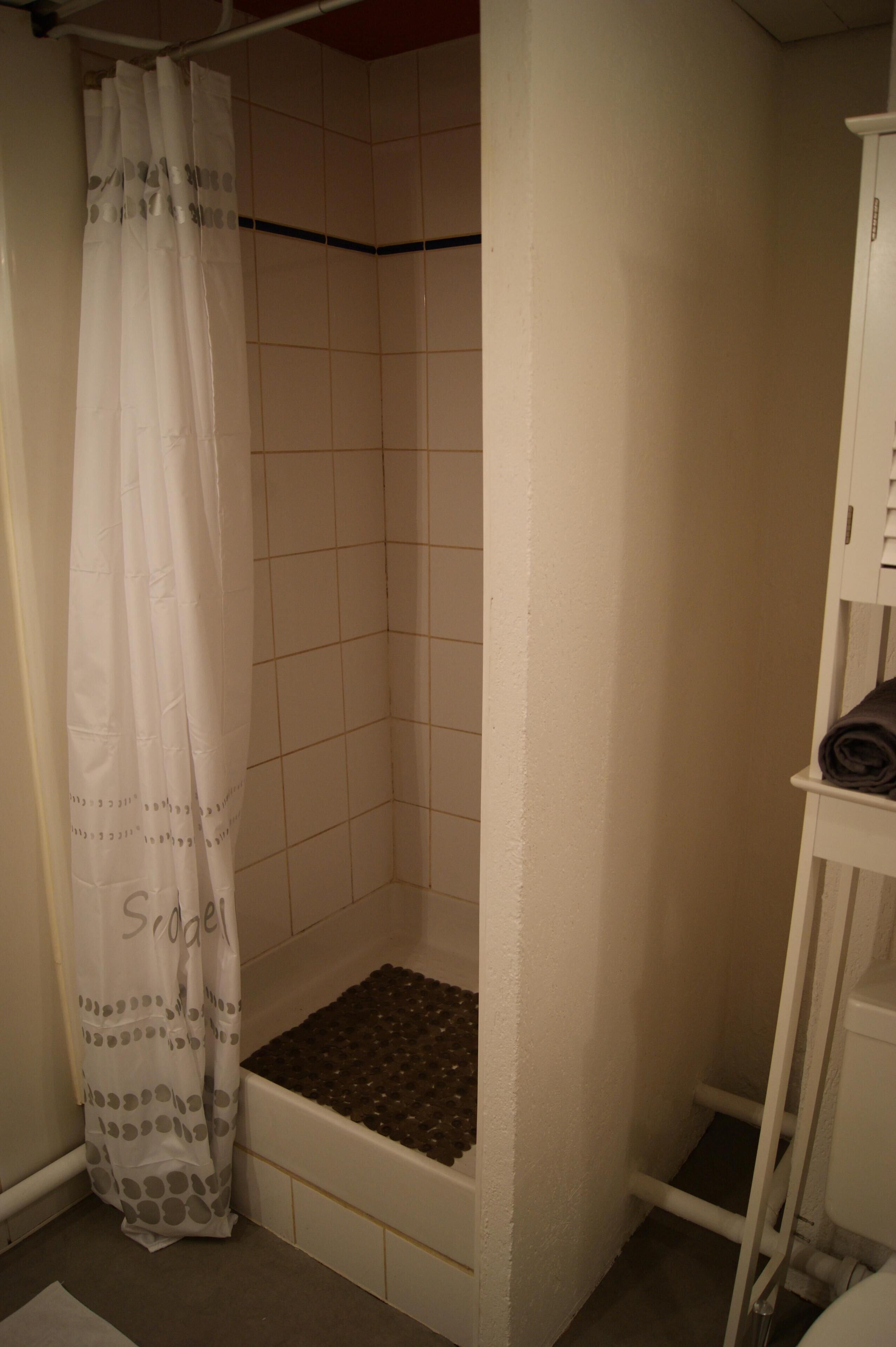A small, enclosed shower area with a white shower curtain and a tiled floor.