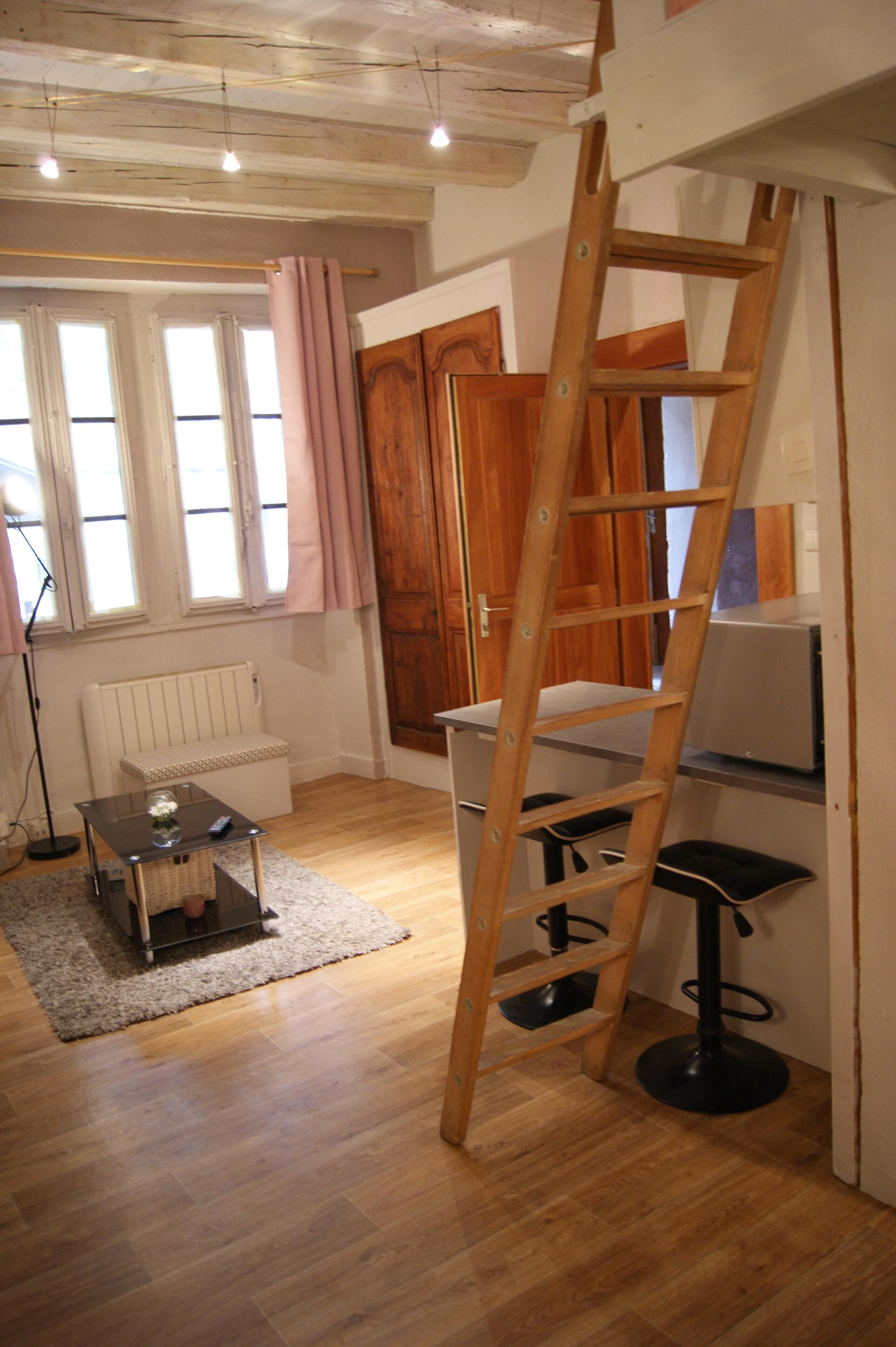 Ein Zimmer mit einer Holzleiter, einem Heizkörper, einem kleinen Tisch mit einer Vase und einem Fenster mit Vorhängen.