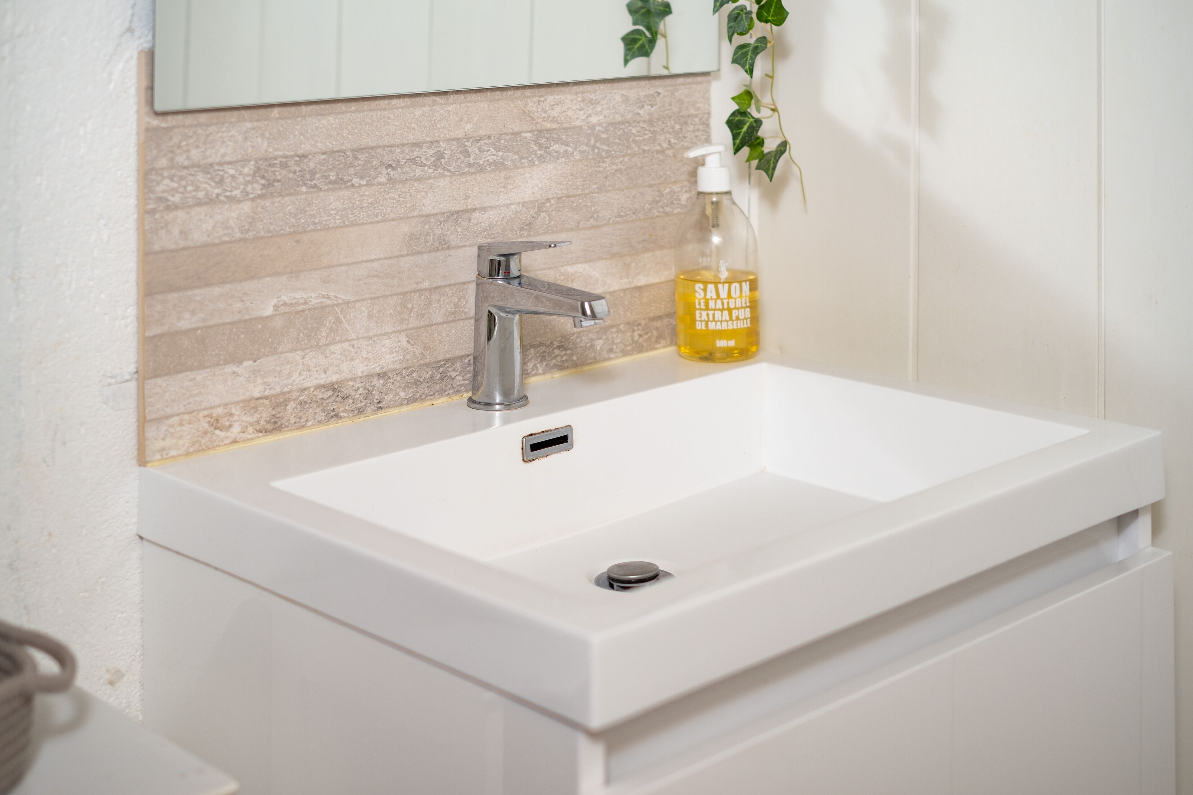 Ein weißes Waschbecken mit modernem Wasserhahn und Seifenspender auf der Ablagefläche.