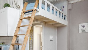 A compact room with a loft bed, a wooden ladder, a kitchenette, and a seating area with cushions. - charming studio in the heart of the old town (Annecy)
