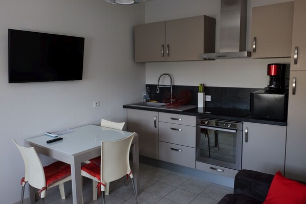 A compact kitchen with a dining area, a flat-screen TV mounted on the wall, and a coffee maker on the counter. - Charming "Potager 2" bungalow in Sologne in a relaxing forest setting (Vouzeron)