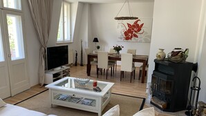 A modern living room with a sofa, coffee table, TV, dining table, chairs, fireplace, and a large window with curtains.