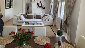 A modern living room with a white sofa, a glass coffee table, and a dining table with woven placemats.