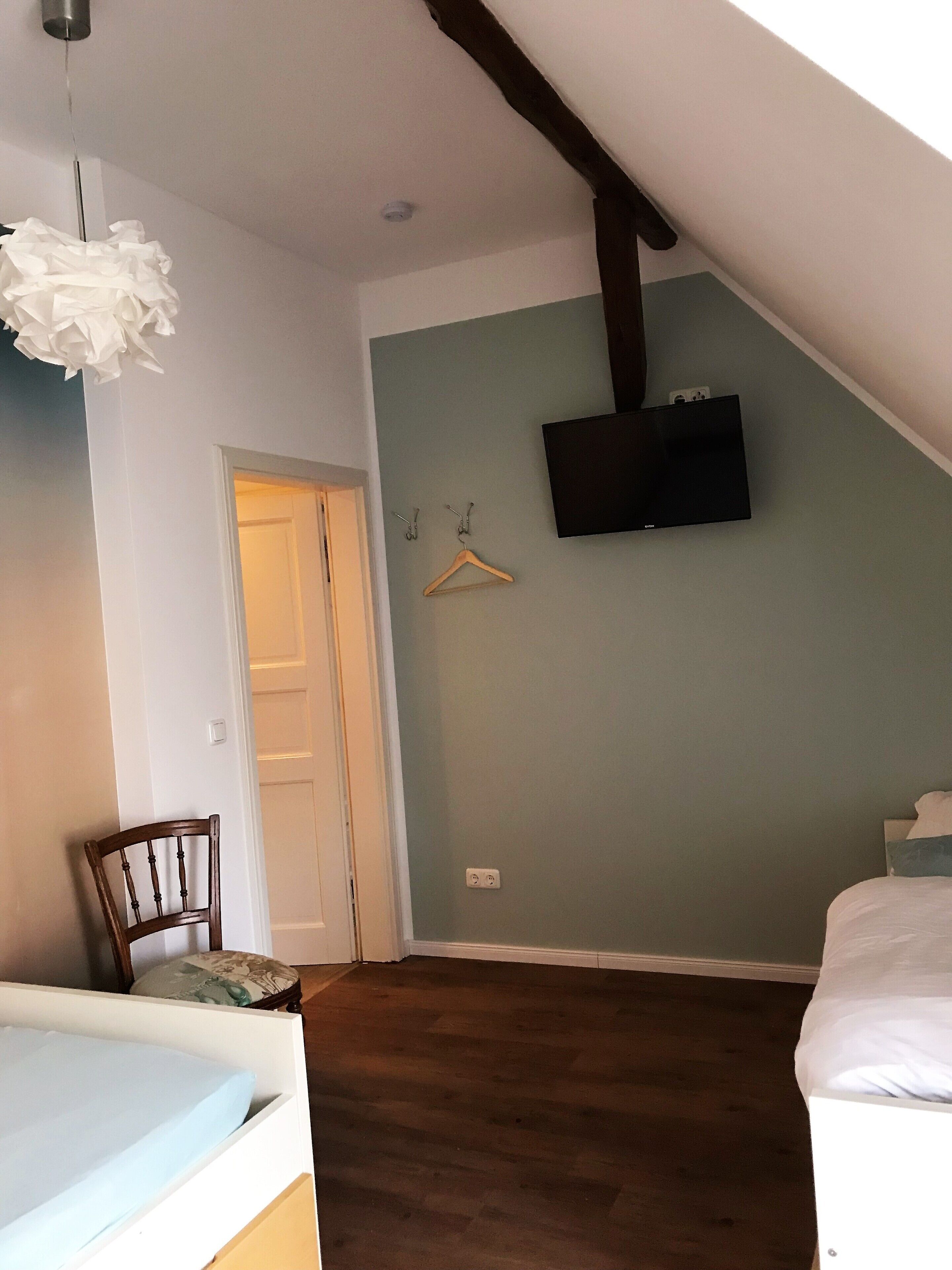 Une chambre avec un plafond en pente, un téléviseur fixé au mur, une chaise en bois et un lit.