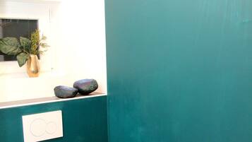 A bathroom with a teal wall, a toilet, a sink with a plant, and a fish decal.