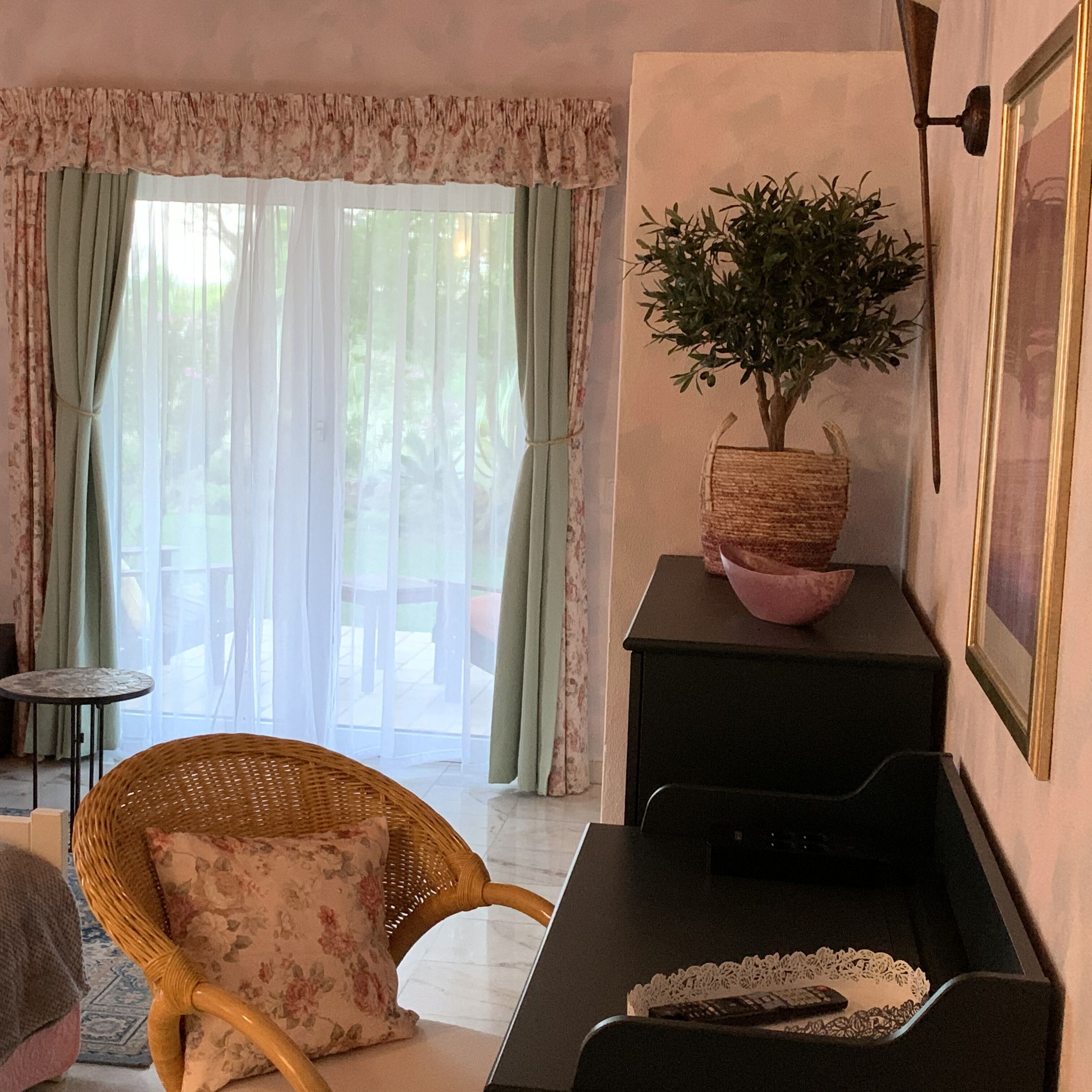 A cozy living room with a wicker chair, a black sideboard, and a potted plant.