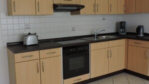 A kitchen with wooden cabinets, a black stove, a sink, and a coffee maker. - Away from the city life and yet part of the action (Appenweier)