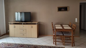 A living room with a TV on a wooden cabinet, a dining table with chairs, and a patterned rug. - Away from the city life and yet part of the action (Appenweier)