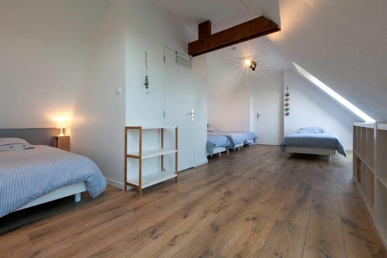 Une chambre avec un plafond en pente, un plancher en bois et un lit recouvert d’une couvre-lit à rayures.