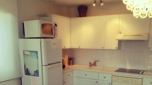 Uma cozinha compacta com armários brancos, micro-ondas, lava-louças e uma mesa de jantar com cadeiras.