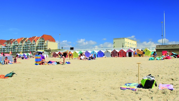 Une plage avec des cabanes de plage aux couleurs vives et, au fond, un bâtiment doté de toits rouges.