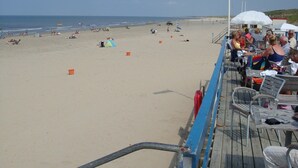 A beachside deck with a flag, beachgoers, and umbrellas.