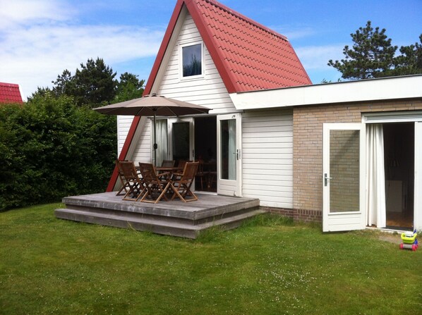 A house with a red roof, a patio with wooden chairs and a table, and a sliding glass door.