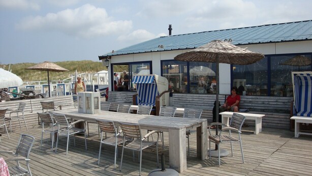 An outdoor dining area with metal chairs and tables, umbrellas, and a building with a blue roof.