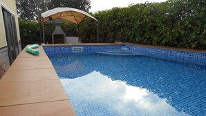 Une piscine aux carreaux bleus, une terrasse en bois et un espace barbecue couvert.