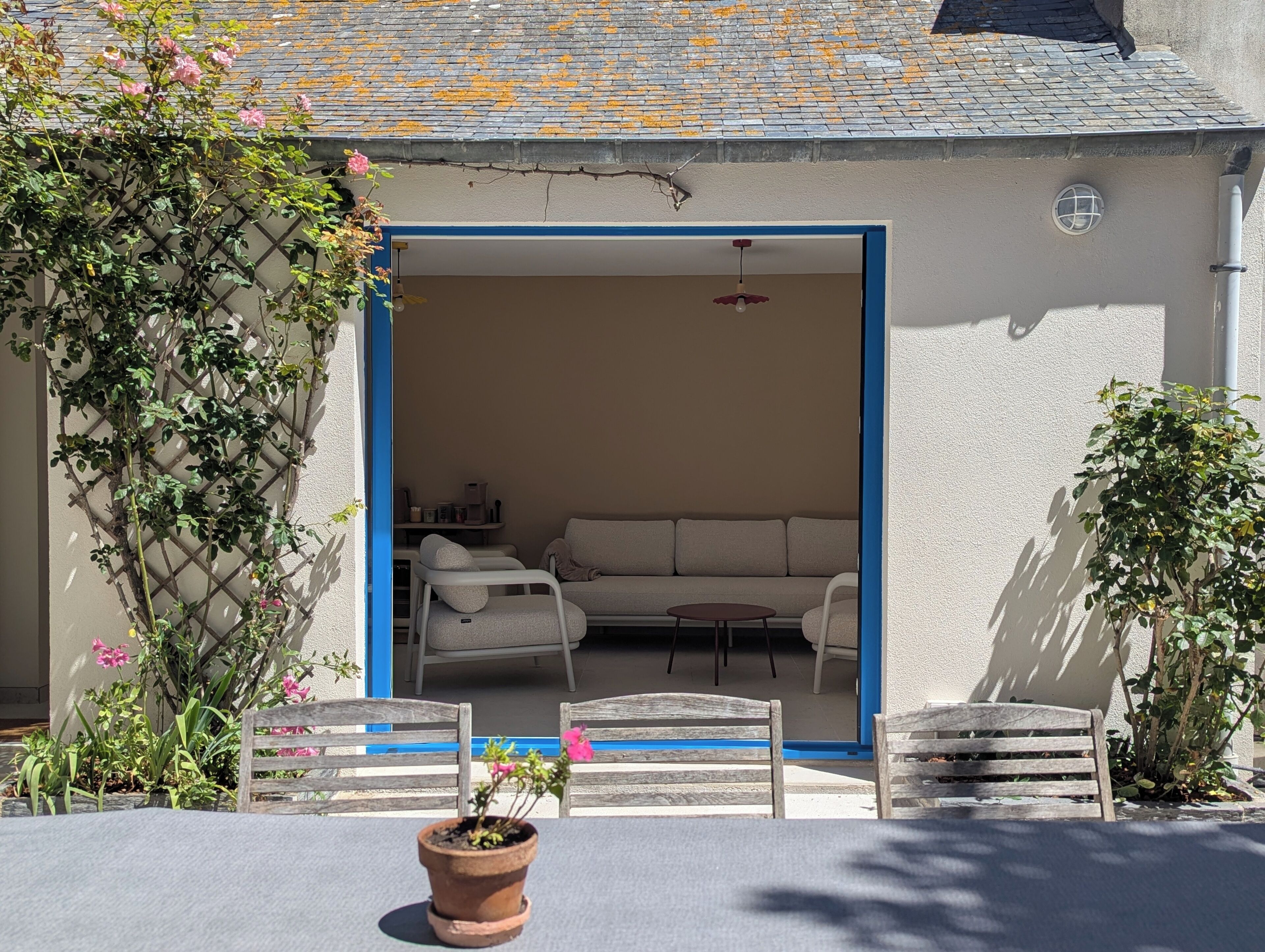 Un espace extérieur aménagé avec un salon de jardin composé d’un canapé et de fauteuils, une plante en pot et un banc en bois.