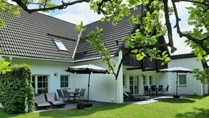 A two-story house with a tiled roof, a covered patio with outdoor furniture, and a well-maintained lawn. - Vacation for the family. Top apartment**** 2-4 persons, 75sqm, terrace. 2 bedrooms.  (Walkenried / Südharz)