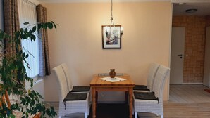 A dining area with a wooden table, two wicker chairs, a potted plant, and a framed picture on the wall. - Vacation for the family. Top apartment**** 2-4 persons, 75sqm, terrace. 2 bedrooms.  (Walkenried / Südharz)