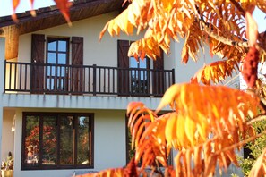 Ein zweistöckiges Gebäude mit Balkon, großen Fenstern und einem sichtbaren Gartenbereich.