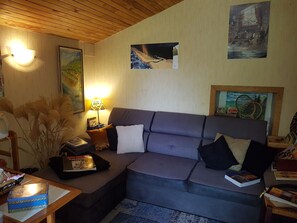 Ein gemütliches Wohnzimmer mit grauem Sofa, einer Lampe, einem gerahmten Gemälde und einem Bücherregal.