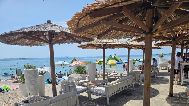 A beachside lounge area with white lounge chairs and thatched umbrellas, overlooking the sea.