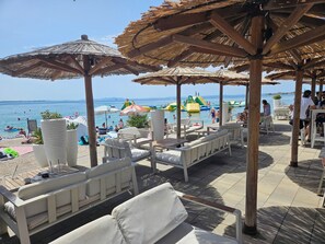Un área de descanso frente a la playa con sillones blancos y sombrillas de paja, con vista al mar.