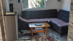 A modern living room with a dark grey sectional sofa, a wooden coffee table, and a large window with a view of greenery.