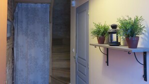 A hallway with a wooden staircase, a door, and a shelf with potted plants and a lantern. - Charming Apartment - Downtown (Châteaubriant)