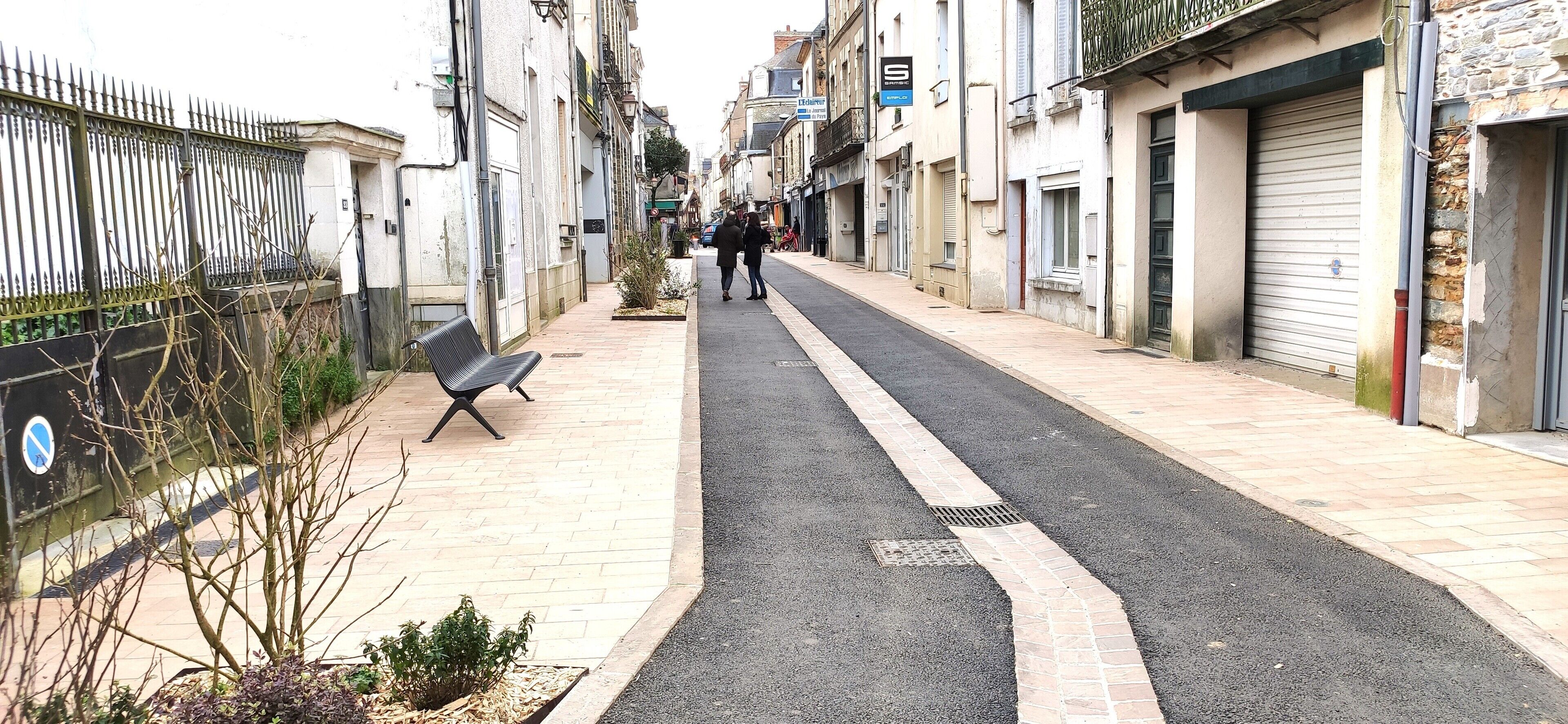 Une rue étroite, avec un banc sur le côté gauche et des boutiques fermées sur le côté droit.