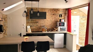 A compact kitchen with a wooden table, black chairs, a built-in oven, and a stone wall backsplash. - Charming Apartment - Downtown (Châteaubriant)
