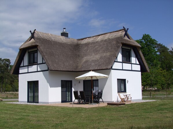 A modern house with a thatched roof, large windows, and a patio area with outdoor furniture.