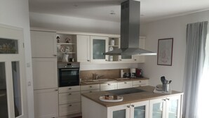 A modern kitchen with white cabinetry, a built-in oven, a stainless steel range hood, and a wooden countertop.