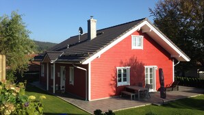 A red house with a chimney, a covered patio, and a lawn.