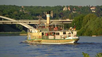A riverboat with a green and white color scheme, a large chimney, and a bridge in the background.